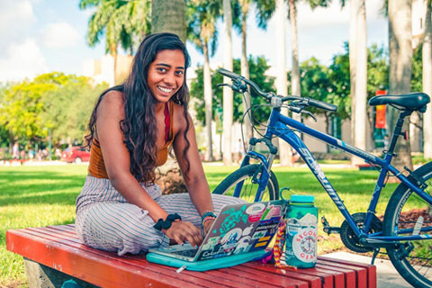 Student sitting outdoors smiling with her laptop and next to a bicycle
