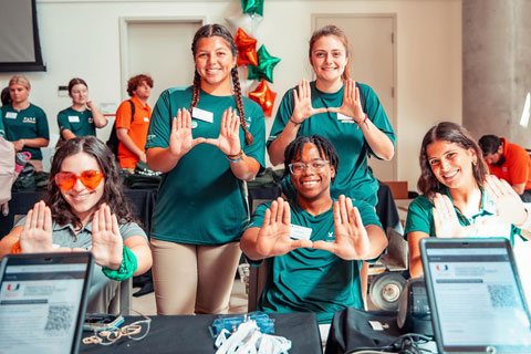 Group of students wearing matching green shirts and doing the U sign with their hands
